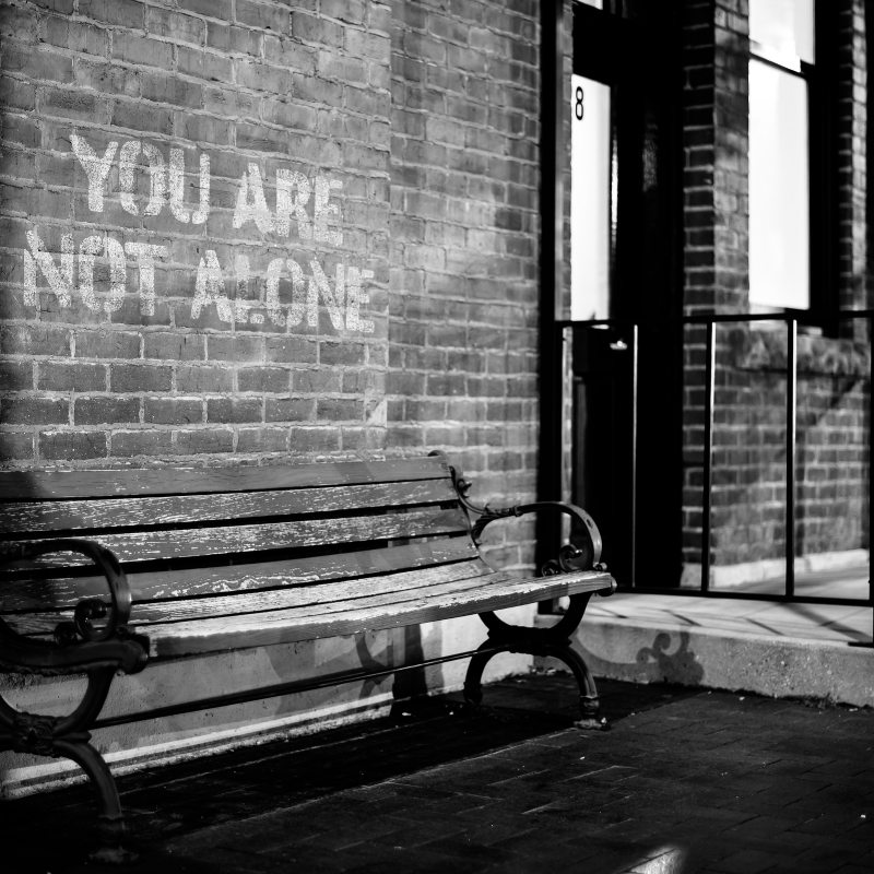 A wooden bench in front of wall with the words YOU ARE NOT ALONE.